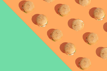Creative pattern made of burgers on bold.orange and green background. Street food and fast food.concept. Minimal flat lay arrangement with copy space.