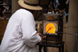 Hombre vestido de blanco y con sombrero de paja elaborando productos artesanales de vidrio soplado en un horno candente en el mercado medieval de Hondarribia en el País Vasco