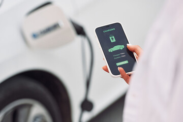 Close up view. Woman charging her electric car and monitoring process on smartphone