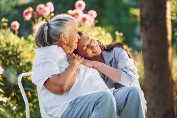 Sitting and embracing each other. Young woman is with her senior mother is in the garden