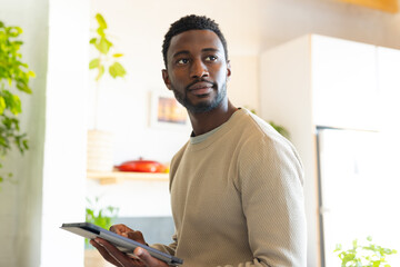 Wall Mural - Happy african american man leaning on countertop in kitchen, using tablet