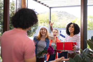 Happy diverse friends greeting at door with gifts at christmas