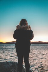 Canvas Print - Vertical shot of a female silhouette standing on the rock looking at the sea at sunset