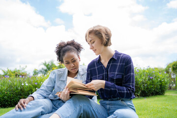 Multi-ethnic students in the park. Two young students read a book in the summer at the park. Preparation for entering university. students read summer books in the park. education