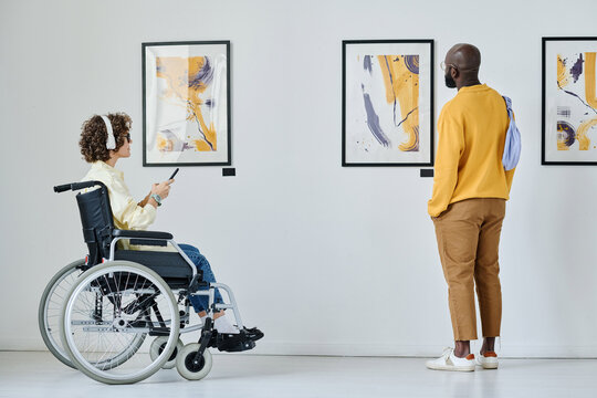 young woman in wheelchair listening to guide with man standing near by while they visiting art galle