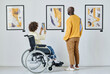 © AnnaStills - Rear view of young woman in wheelchair taking photo on mobile phone while visiting art gallery with man
