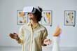 © AnnaStills - Young girl standing and gesturing in virtual reality glasses visiting virtual art gallery