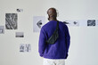 © AnnaStills - Rear view of African young man in wireless headphones listening to guide and watching photos on the wall