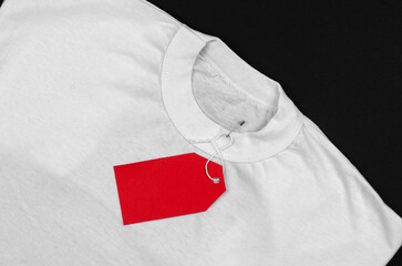 White t-shirt on a black background with a red blank label. Empty red price tag on a white t-shirt.