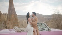 Beautiful Bride And Groom In Wedding Dress And Suit Near Pink Vintage Cabriolet Car. Action. Wedding Couple Standing Near A Convertible On A Natural Background.