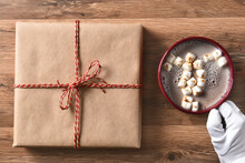 Santa Claus Hand With A Mug Of Cocoa And A Plain Brown Paper Wapped Christmas Present.
