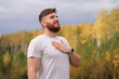 © Евгений Шемякин - young bearded relaxed calm man enjoying good weather in the forest, autumn park, breathing deep fresh air and smiling. Guy with beard holding his hand on chest, heart with his eyes closed