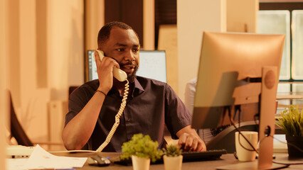 Poster - Executive assistant answering landline phone call in office with big windows, having remote conversation on telephone with cord. Chatting on phone line with coworkers, communication.