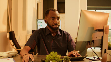 Poster - African american man working on research project with computer, analyzing data report to create presentation. Brainstorming ideas to plan management paperwork in office during sunset.
