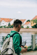 © Masson - Backside view on man in green shirt with backpack and mobile phone walking near river in Wroclaw, Poland