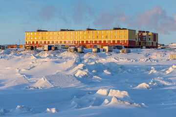 Wall Mural - A small northern village in the Arctic. Residential buildings and fishing sheds on the coast of the frozen sea. Cold frosty winter weather. Ice hummocks and snow. Chukotka, the Far North of Russia.