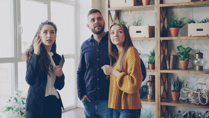 Wall Mural - Confident realtor is describing advantages of new house to young couple looking around, talking and smiling. Husband and wife are excited about new accommodation.