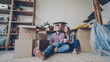 © silverkblack - Adorable young couple is talking and holding mugs while sitting on floor of new flat after relocation. Numerous boxes, packed furniture and plants are visible.