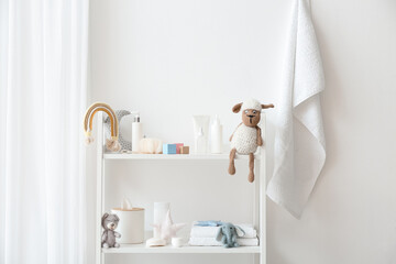 Shelf unit with bath supplies for children and toys near white wall in bathroom