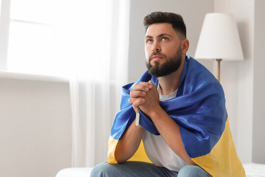 Young man with flag of Ukraine praying in bedroom