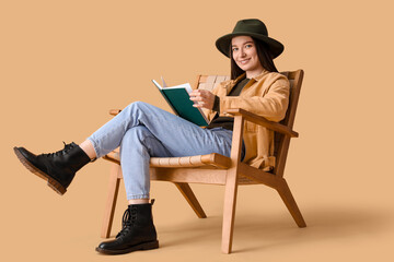 Wall Mural - Young woman reading book in armchair on beige background