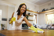 Home cleaning, black woman and kitchen counter with housekeeper with gloves to disinfect spray for happy spring clean day at home. Hygiene housework of female from UK with smile ready for tidy house