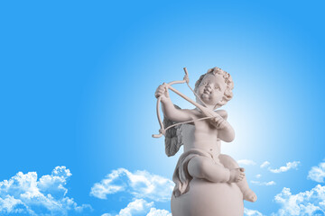 Figurine of an angel Cupid on the podium with a bow and arrow on a blu sky with clouds background . Valentine's Day.