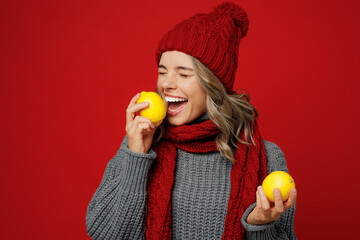 Wall Mural - Young smiling happy woman wear grey sweater scarf hat hold biting citrus lemon fruit isolated on plain red background studio portrait. Healthy lifestyle ill sick disease treatment cold season concept.