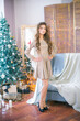 A cute teenage girl with long curly hair in a shining dress in a room decorated for Christmas with shining garlands. Christmas mood. beauty and fashion