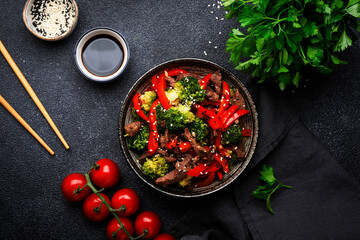 Wall Mural - Stir fry vegetables with beef, paprika and broccoli with sesame seeds in bowl on black table  background, top view