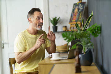 Remote university mature student taking distance classes. Focused handsome beard man sitting at desk at home with laptop computer, gesturing on video meeting. Remote education, studying online concept