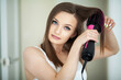 Woman drying long hair with hair dryer round brush.