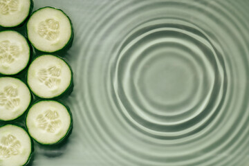 Wall Mural - Cucumber slices lie on surface of rippled transparent fresh green water gel with fleck, waves, shadow, expanding circles