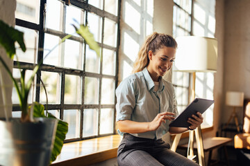 Smiling business girl, doing her work, being at the workplace, using a tablet.