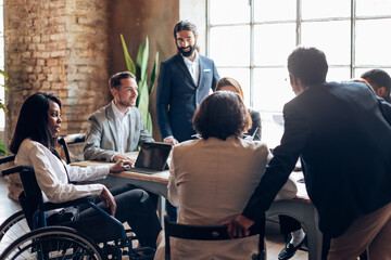 african american businesswoman sitting in wheelchair brainstorming at table with other colleagues