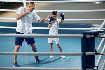 Two athletes, son and father is doing sports in gym. Beginner boxer workout with his coach ar boxing ring, indoors. Sport, power, energy and active lifestyle