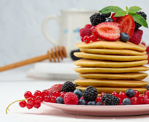 Wall Mural - Stack of baked pancakes with fruits in a round plate on a white table, delicious breakfast