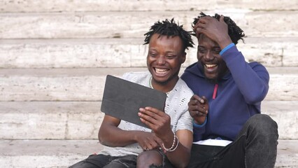 laughing together: african friends have fun watching a video on tablet