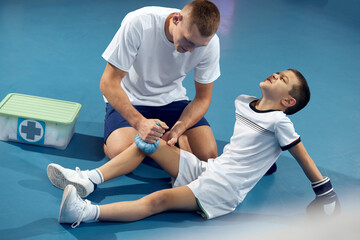 Personal coach, team trainer provides first aid to an athlete with a leg injury. Boxing training in the gym. Sport, medicine, studying