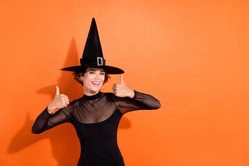 Wall Mural - Photo portrait of gorgeous young lady show double thumb up smile wear stylish black halloween witch clothes isolated on orange background
