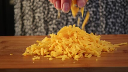 Wall Mural - woman hand showing shredded cheddar cheese on wooden board close up