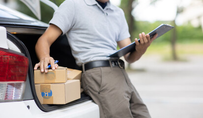 A delivery man is delivering cardboard boxes to customers at the door of a private car. young man delivery man in casual clothes Parcel moving service