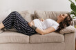 © Look! - Happy curly woman in striped black pants and white tee lies on beige sofa and smiles. Pregnant lady gently touches belly