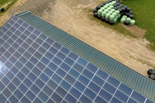 Aerial View Of Blue Photovoltaic Solar Panels Mounted On Farm Building Roof For Producing Clean Ecological Electricity. Production Of Renewable Energy Concept