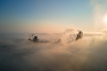 Poster - Aerial view of cement factory with high concrete plant structure and tower crane at industrial manufacturing site on foggy evening. Production and global industry concept