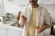 © LIGHTFIELD STUDIOS - partial view of smiling bearded man with glass of white wine using smartphone in blurred kitchen.