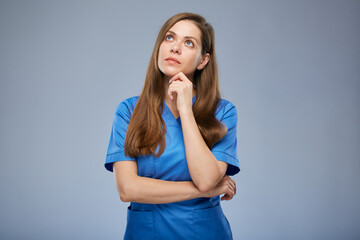 Wall Mural - Serious thinking nurse woman in blue medical uniform looking up. Isolated female portrait.