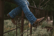 Western Lifestyle Concept With Person Sitting On Fence In Cowboy Boots.