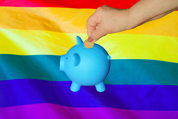 Hand of elderly woman putting coin into piggy bank on LGBT flag background. Hand putting coin to piggy bank. Retirement savings, piggy bank. Concept saving money and retirement fund in LGBT