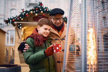 Wall Mural - Little boy and his grandfather drink tea by the fire at Christmas market.